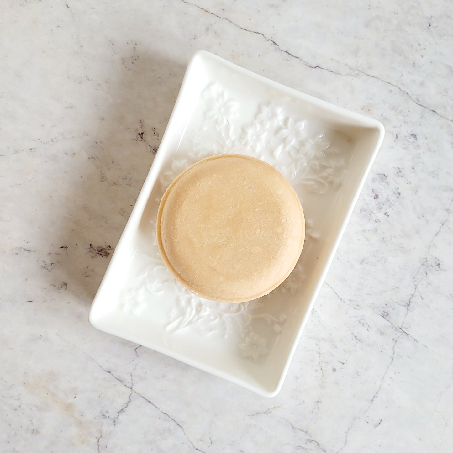 Pink solid shampoo bar. pink round disk, in white ceramic soap dish. plastic free packaging.